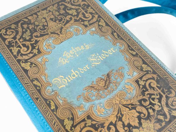 Tasche aus einem Buch von Heine "Buch der Lieder" in hellblau/petrol gehalten mit goldenen Ornamenten am Cover kombiniert mit braun/petrol gemusterter Krawatte und petrolfarbenem Stoff