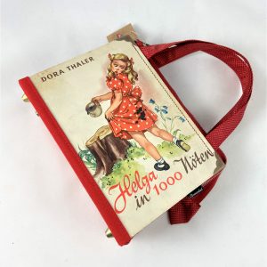 Tasche aus einem Jugendbuch "Helga in 1000 Nöten" mit einem Mädchen am Cover, das sich am Kleidchen mit Heidelbeeren angepatzt hat, kombiniert mit einer hellroten Krawatte