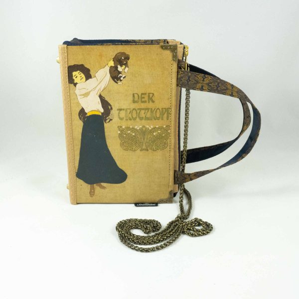 Tasche aus einem alten Buch "Der Trotzkopf" in beige. Am Cover ist eine Frau, die ein Hündchen in die Höhe hält, zu sehen. Buch kombiniert mit einer dunkelblau/goldenen Krawatte und goldenem Stoff.