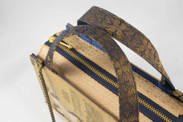 Tasche aus einem alten Buch "Der Trotzkopf" in beige. Am Cover ist eine Frau, die ein Hündchen in die Höhe hält, zu sehen. Buch kombiniert mit einer dunkelblau/goldenen Krawatte und goldenem Stoff.