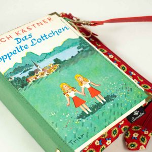 Tasche aus einem Buch von Erich Kästner "Das doppelte Lottchen" mit den Zwillingen am Cover auf einer grünen Wiese, kombiniert mit einer rot/grün/blau blumig gemusterten Krawatte, roter Taschenriemen