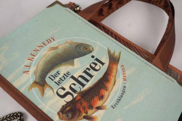 Tasche aus einem Buch "Der letzte Schrei" mit zwei Fischen am Cover in hellblau und goldbraun gehalten, kombiniert mit einer Krawatte in goldbrauner Farbe, die auch Fische abbildet