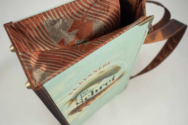 Tasche aus einem Buch "Der letzte Schrei" mit zwei Fischen am Cover in hellblau und goldbraun gehalten, kombiniert mit einer Krawatte in goldbrauner Farbe, die auch Fische abbildet