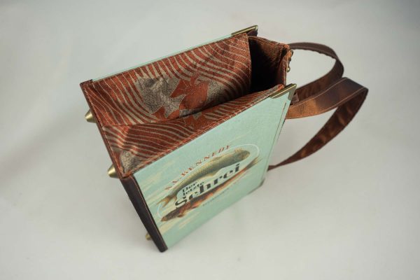Tasche aus einem Buch "Der letzte Schrei" mit zwei Fischen am Cover in hellblau und goldbraun gehalten, kombiniert mit einer Krawatte in goldbrauner Farbe, die auch Fische abbildet